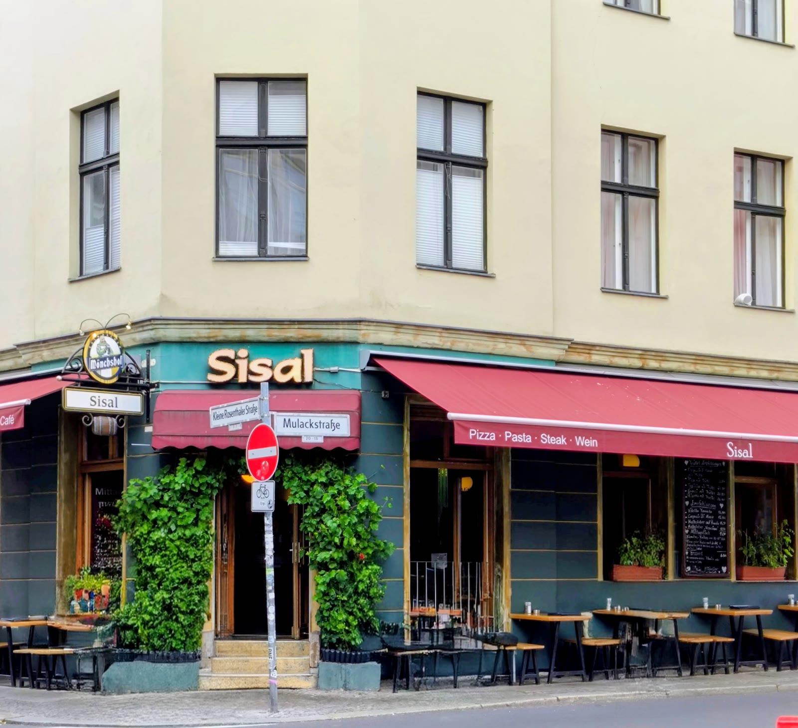 Die Fassade am Tag mit roter Markise und Efeu