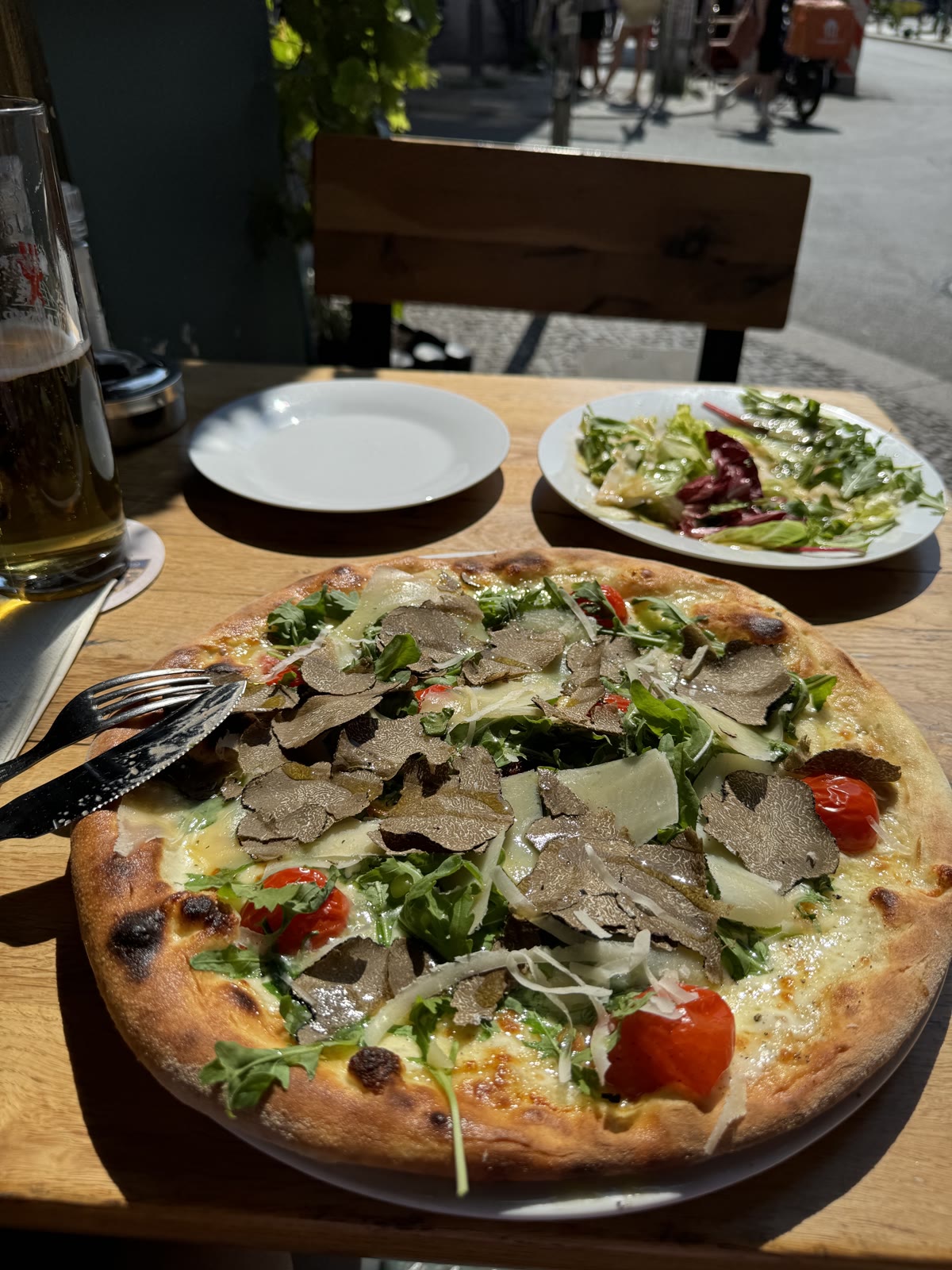 Pizza mit Rucola und Tomaten und ein kleiner Salat auf einem Tisch draußen bei Tageslicht