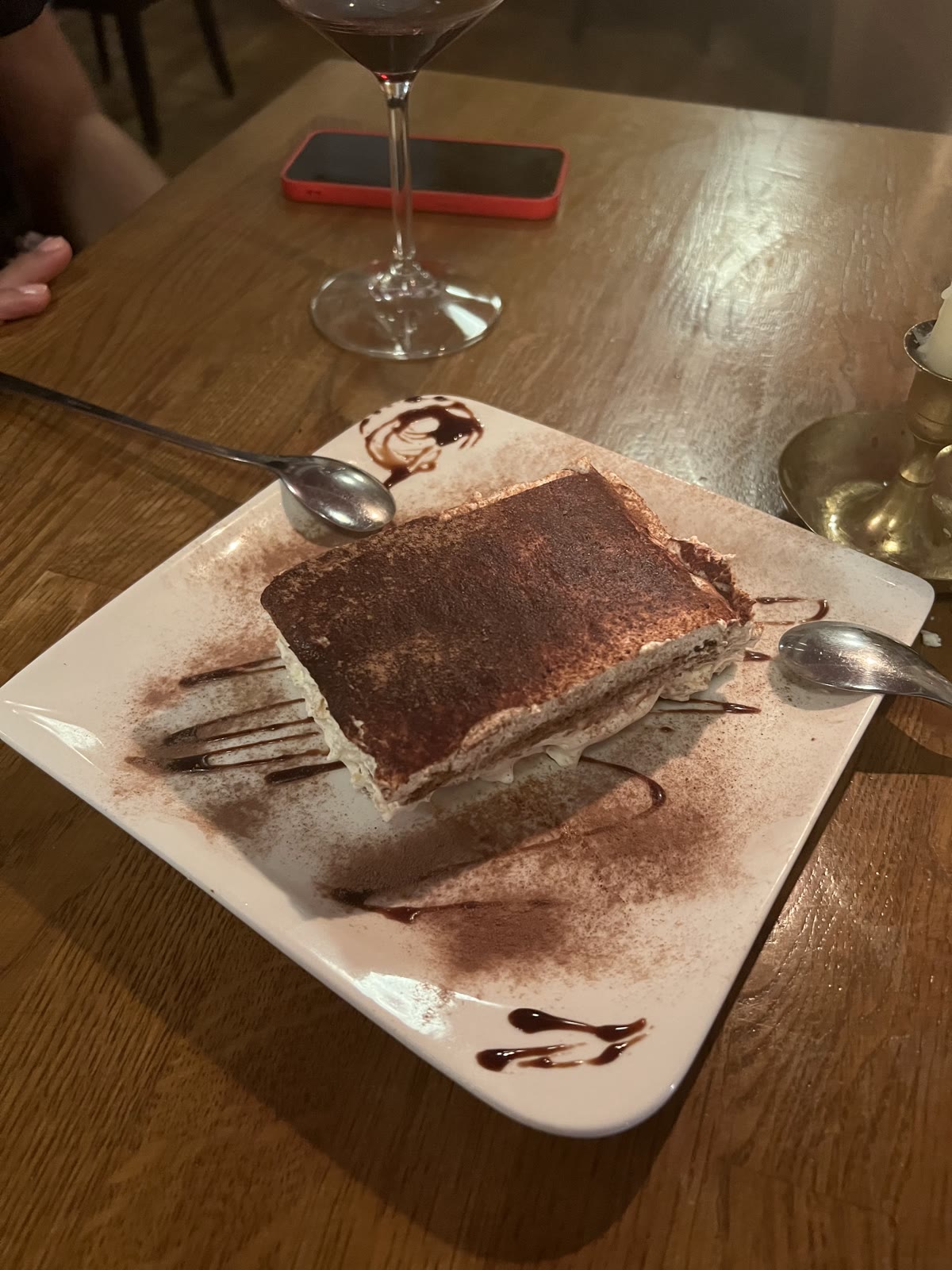 Hausgemachtes Tiramisu mit Kakao auf einem quadratischen Teller, dahinter ein Glas Rotwein und eine Kerze